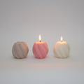 Twisted sphere soy candle on grey concrete surface with white wall background
