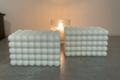 Two white bubble texture square candles on grey surface