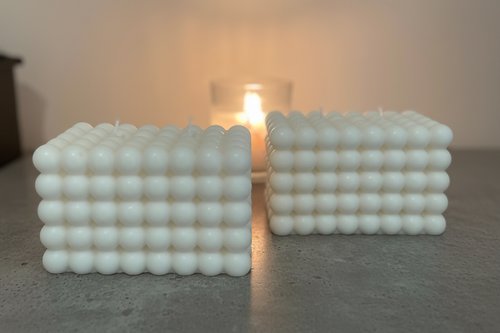 Two white bubble texture square candles on grey surface